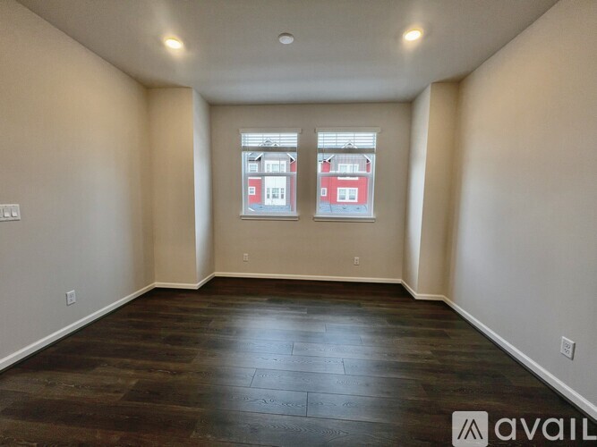 A spacious room with dark wood flooring and a window showing a red building outside.
