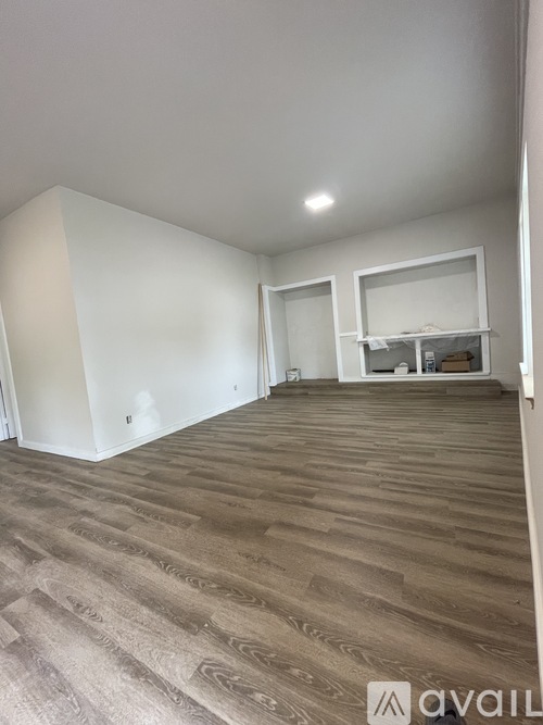 A room with wooden flooring and a white wall with a mirror and shelves.
