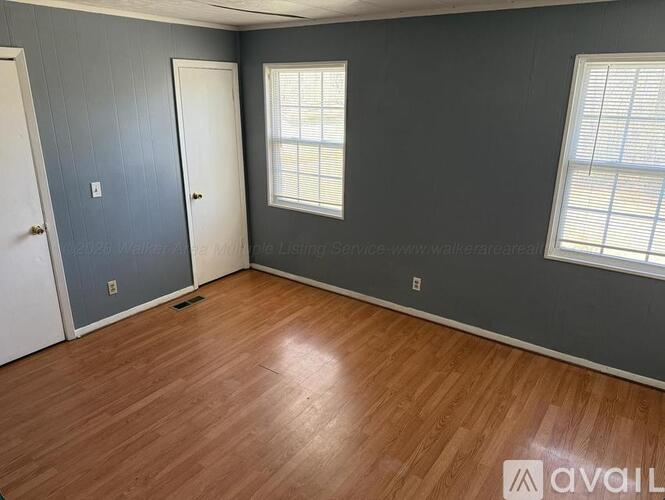 A room with wooden flooring and two windows.