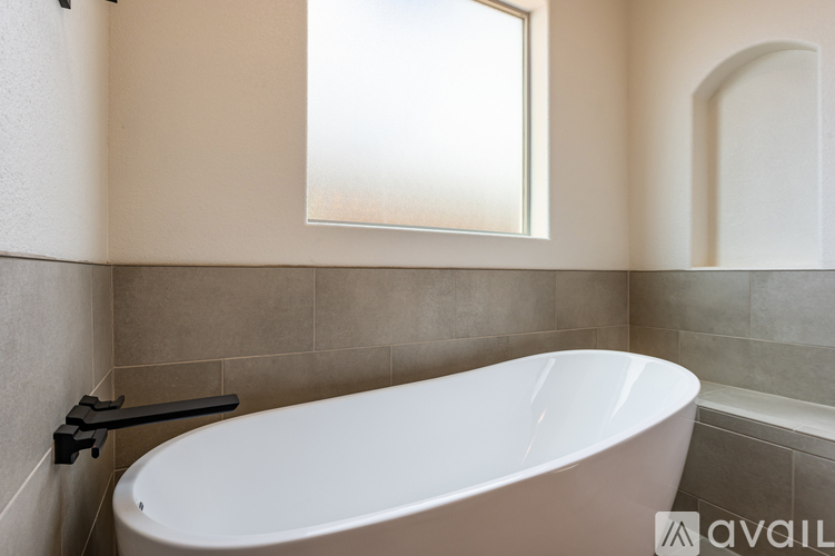 A white bathtub in a bathroom with a window above it.