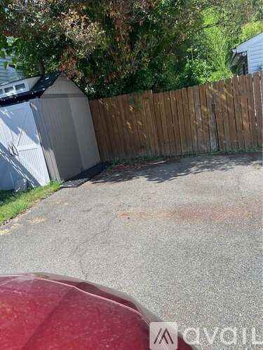 A red car is parked in front of a wooden fence.