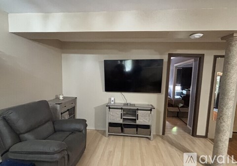A living room with a grey couch, a television, and a wooden floor.
