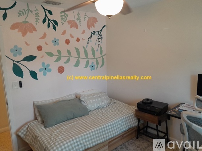 A bedroom with a bed, a desk, and a wall mural of flowers and leaves.