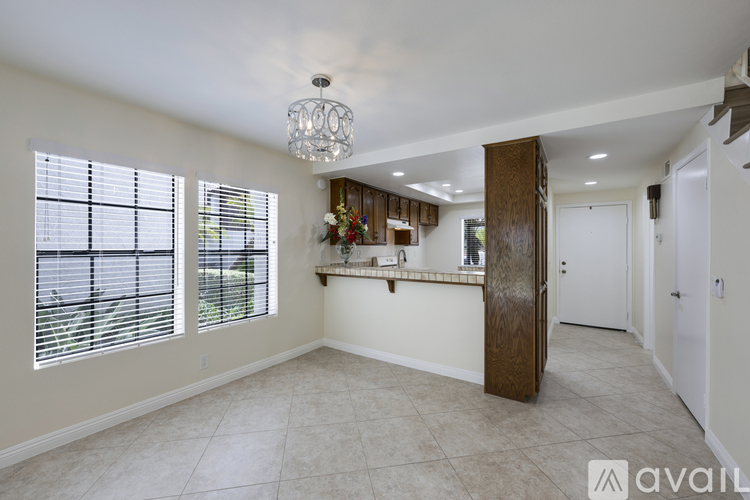 A spacious room with a chandelier, a window with blinds, and a wooden door leading to another room.