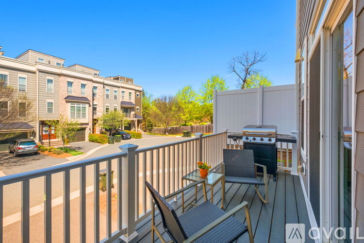 A balcony with a table and chairs overlooks a building and a tree.