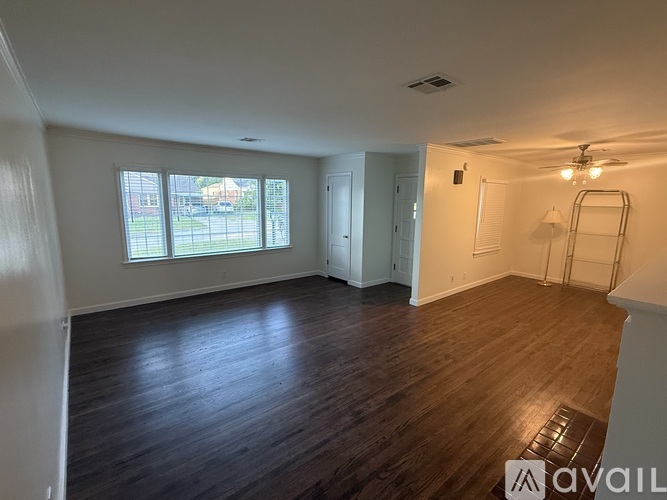 A room with wooden floors and white walls, with a window showing a view of a street.