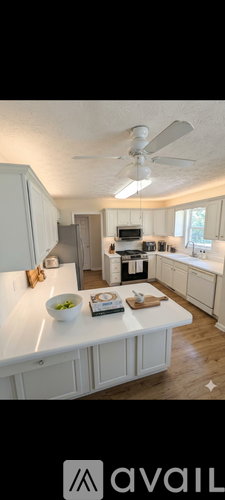A kitchen with a white ceiling fan and a white table with a bowl of fruit on it.