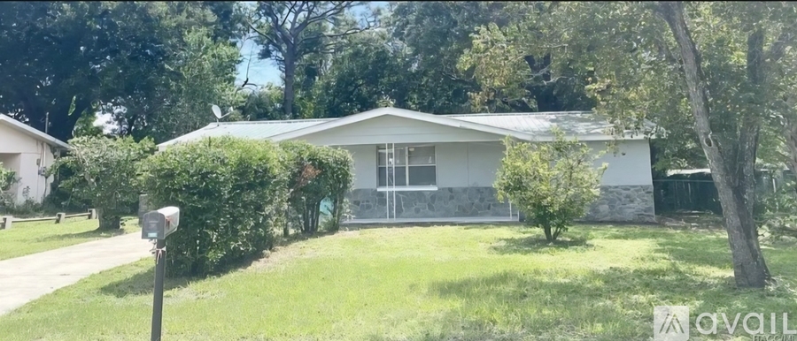 A house with a white exterior and a grey roof is surrounded by greenery.