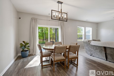 A living room with a wooden table and chairs, a couch, and a large window with curtains.