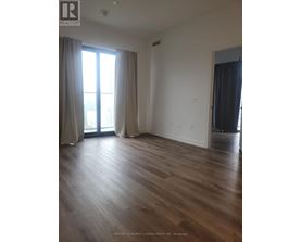 A room with wooden flooring and a large window with curtains.