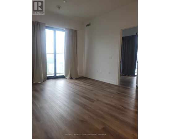 A room with wooden flooring and a large window with curtains.