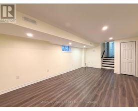A spacious room with wooden flooring and a staircase in the background.