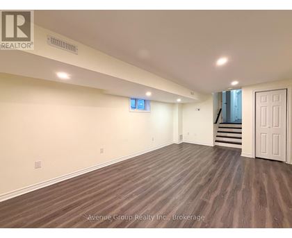 A spacious room with wooden flooring and a staircase in the background.
