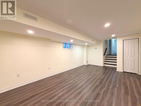 A spacious room with wooden flooring and a staircase in the background.