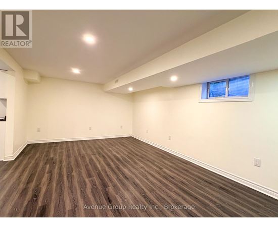 A spacious room with wooden flooring and a window with a blue sky view.
