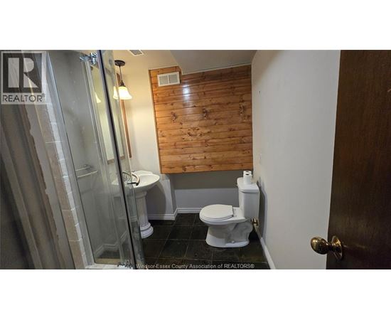 A bathroom with a wooden panel wall and a glass shower door.