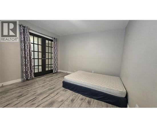 A bedroom with a bed, wooden flooring, and a window with curtains.