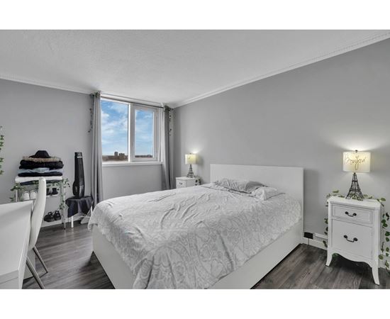 A bedroom with a large bed, a chair, and a small table with a lamp.