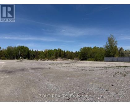A large, empty parking lot with a fence and trees in the background.