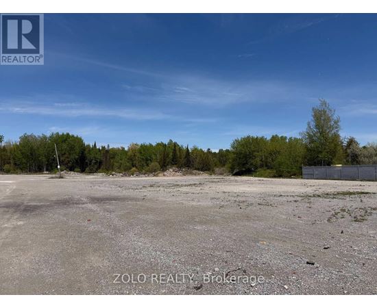 A large, empty parking lot with a fence and trees in the background.