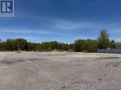 A large, empty parking lot with a fence and trees in the background.