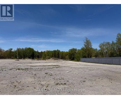 A barren land with trees in the background and a fence on the right side.