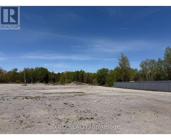 A barren land with trees in the background and a fence on the right side.