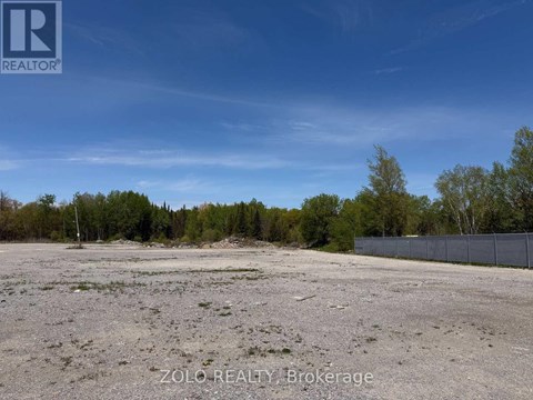A barren land with trees in the background and a fence on the right side.