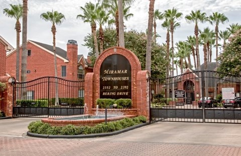 The entrance to Miramar Townhomes is surrounded by a black fence and palm trees.
