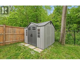 A grey shed with a black roof is situated in a grassy area.