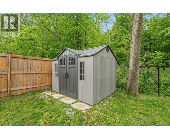 A grey shed with a black roof is situated in a grassy area.