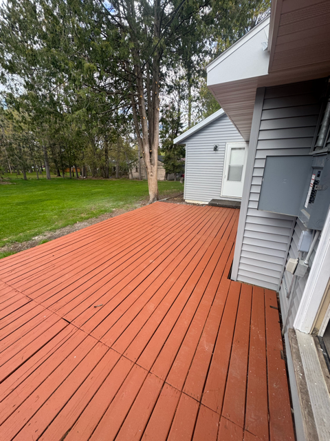 A wooden deck is in front of a house and trees.