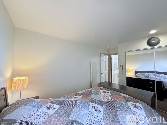 A bedroom with a bed covered in a quilt and a lamp on the side table.