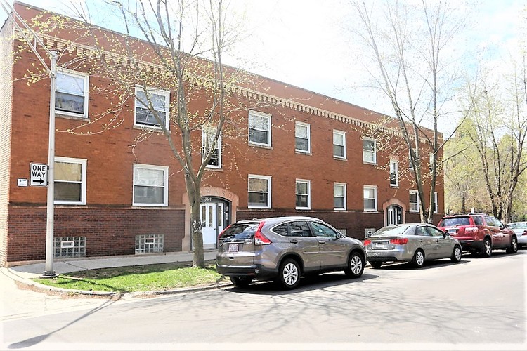 A street view of a red brick building with cars parked in front.