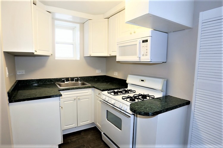 A kitchen with white cabinets and black countertops.