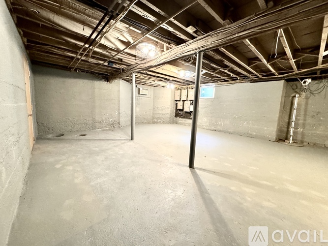 A spacious basement with concrete walls and ceiling, and exposed pipes running along the ceiling.