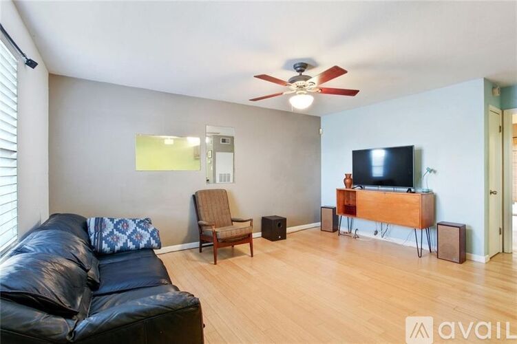 A living room with a black leather couch, a wooden chair, a television, and a ceiling fan.