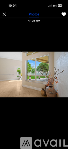 A room with a window showing a view of trees and a vase with dried flowers on a table.