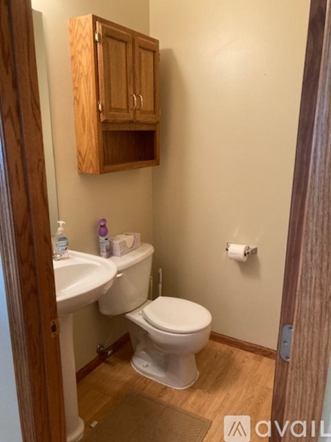 A small bathroom with a toilet, sink and wooden cabinet.