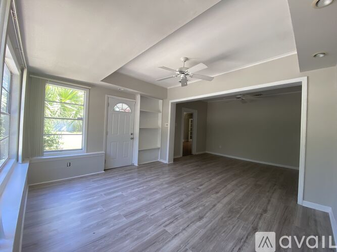 A spacious room with a ceiling fan and lighting, featuring a window with a view of greenery outside.