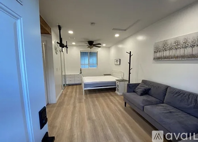 A living room with a grey couch and a bed in the background.