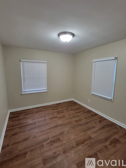 A room with wooden flooring and two windows.