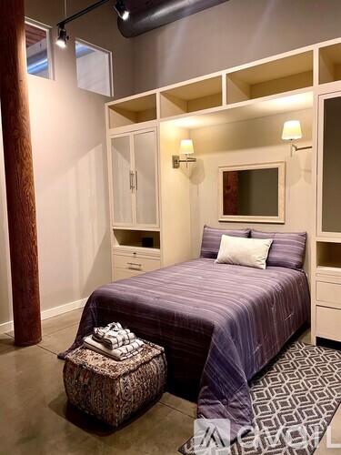 A bedroom with a purple bedspread and a small ottoman.