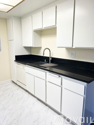 A kitchen with white cabinets and a black counter top.