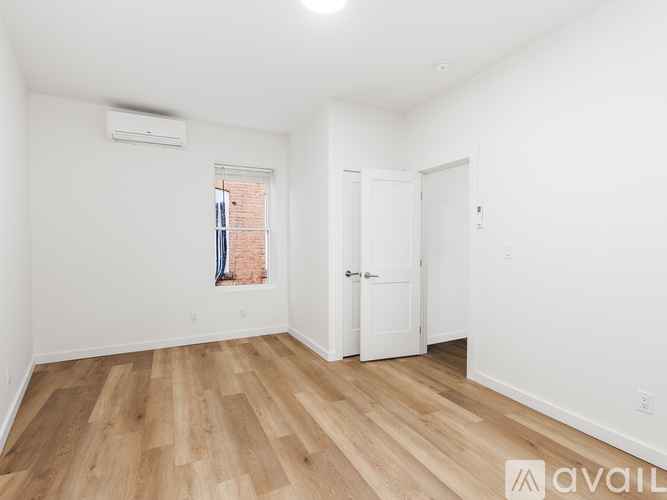 A room with wooden flooring and a window with a view of a brick building outside.
