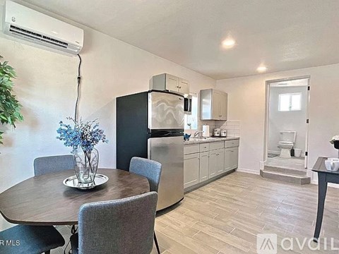 A kitchen with a table and chairs in the foreground and a refrigerator, microwave, and cabinets in the background.