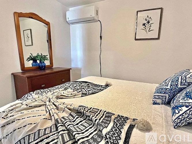 A bedroom with a bed, a dresser, a mirror, and a wall-mounted air conditioner.