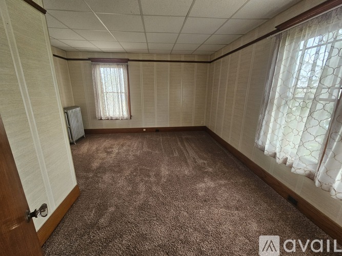 A room with a carpeted floor and a window with curtains.