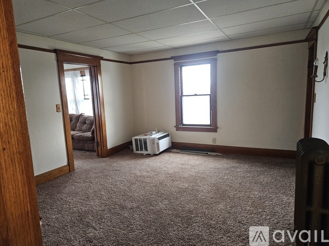 A room with a carpeted floor, a window, and a door leading to another room.