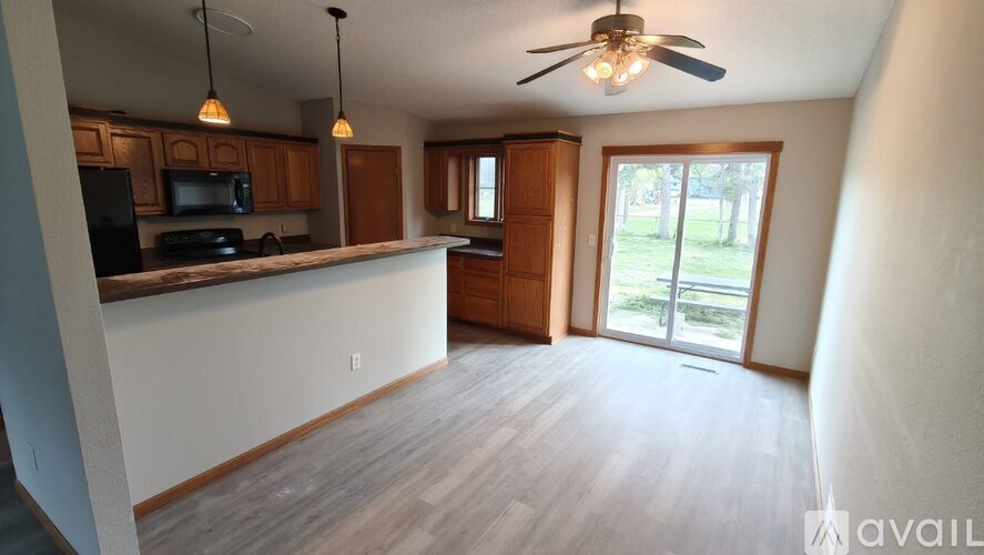 A kitchen with a black fridge and microwave, wooden cabinets, a ceiling fan, and a sliding glass door leading to a grassy area.